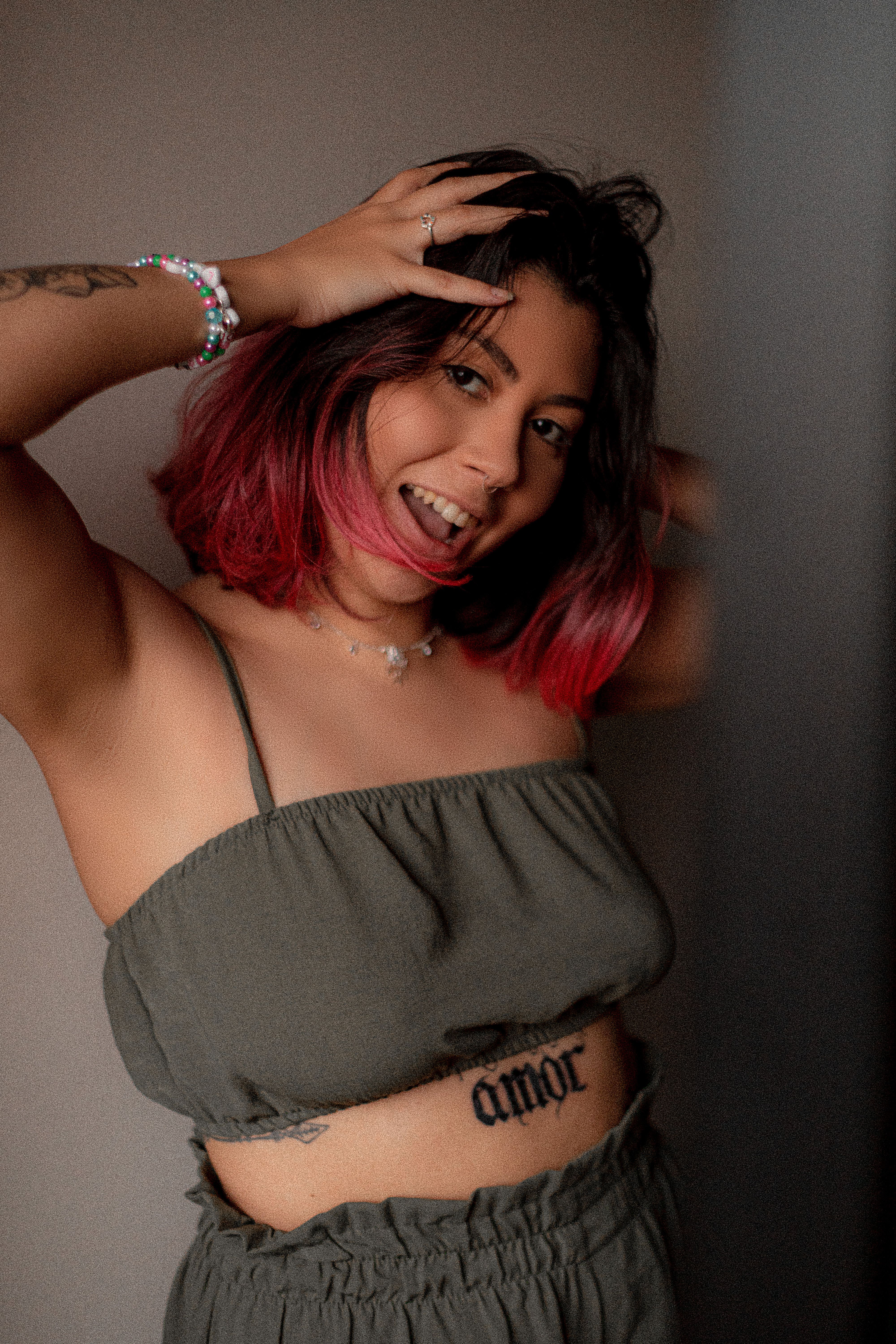 Smiling woman with pink hair and tattoos poses confidently indoors.