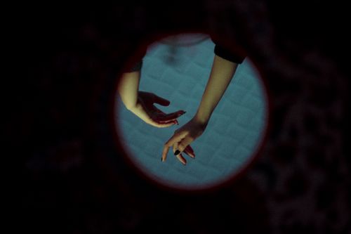 Free A creative close-up photograph of hands reaching, viewed through a circular frame in low light. Stock Photo