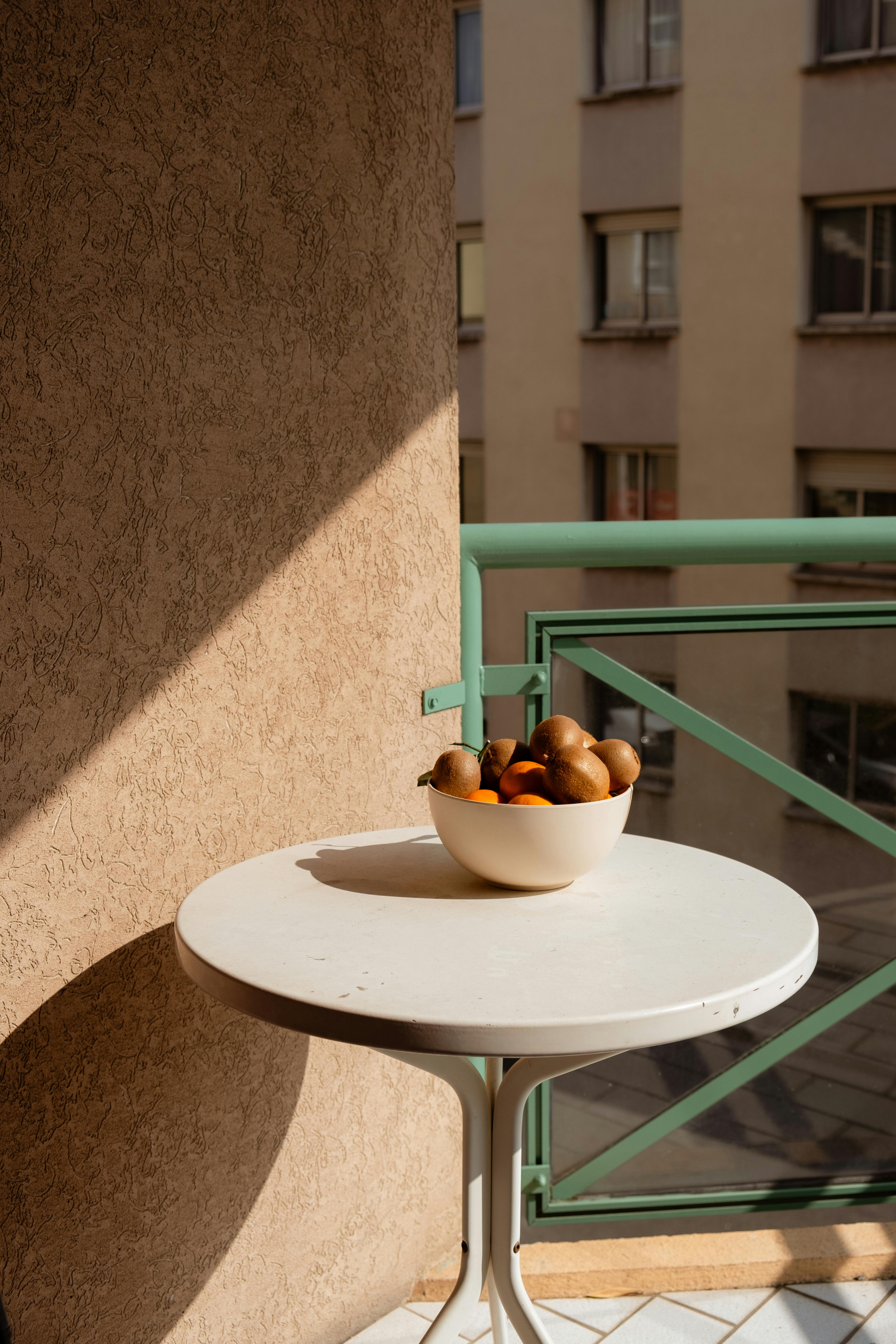 Free A serene balcony scene with a bowl of fresh fruit casting shadows in warm daylight. Stock Photo