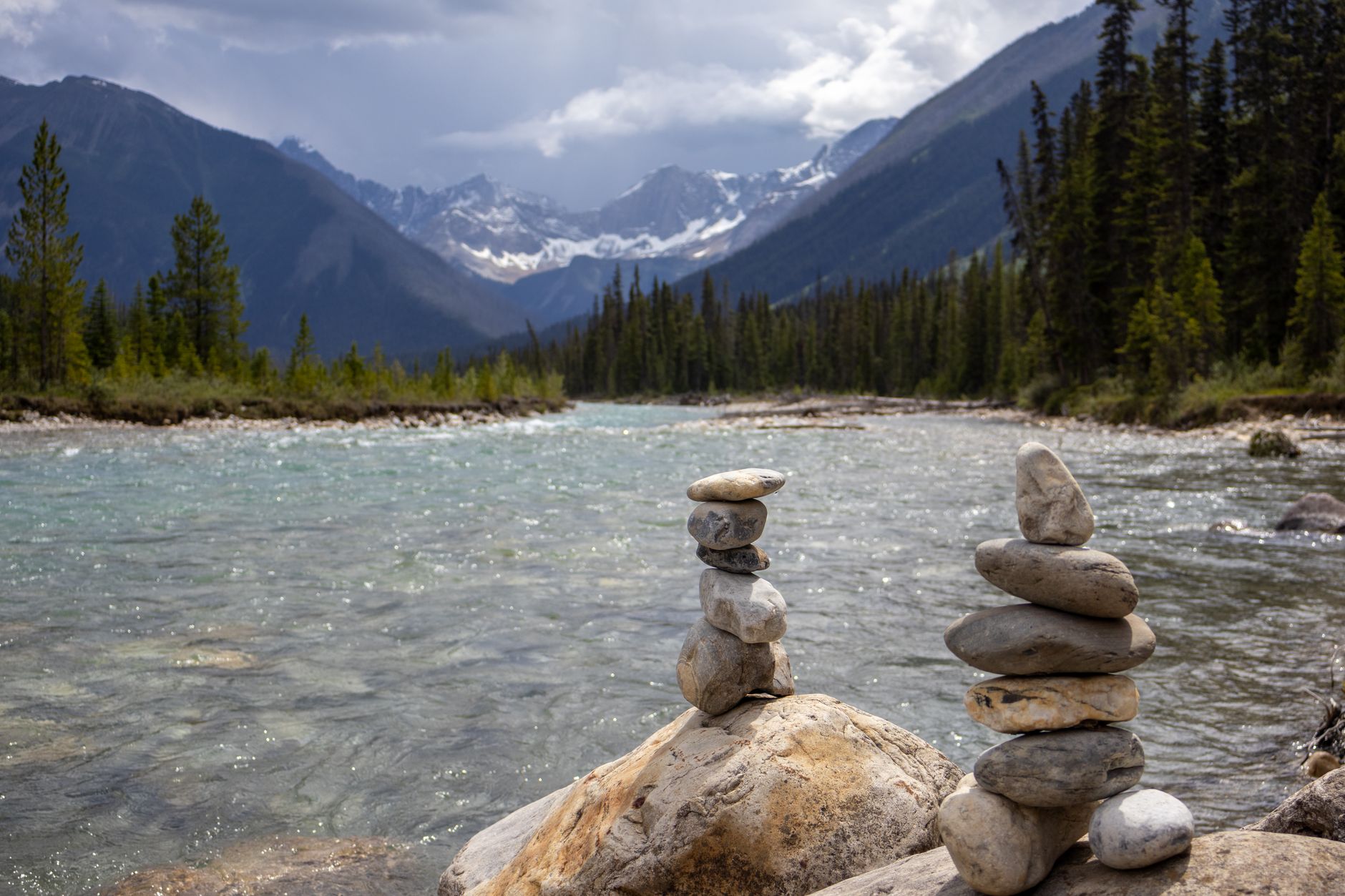 Serene river in Banff National Park with stacked stones and majestic mountains.