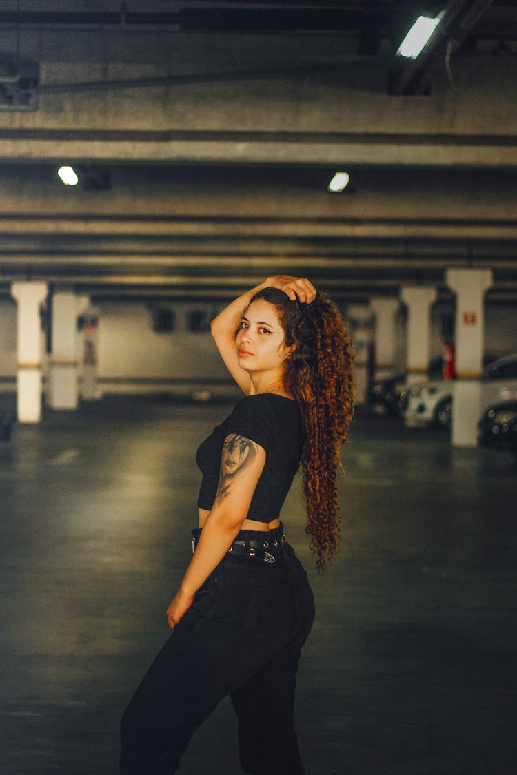 Woman In A Black T-Shirt And Pants Posing In An Underground Parking Garage 