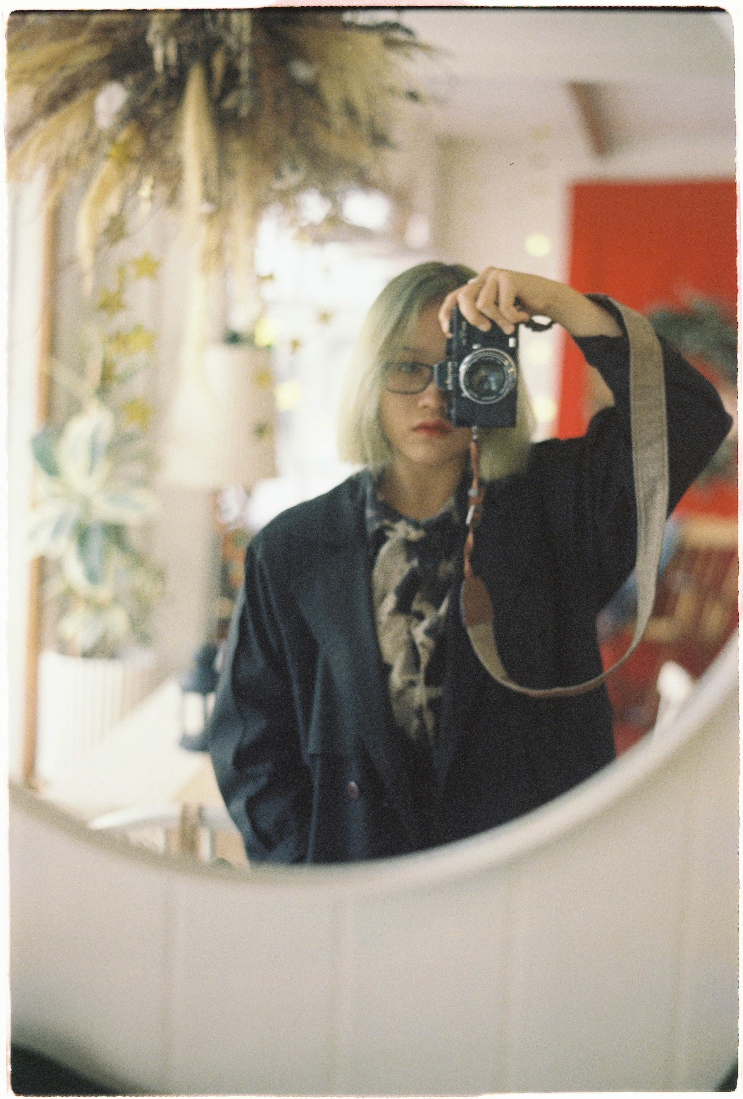 A woman captures her reflection with a camera in an artistic indoor setting.