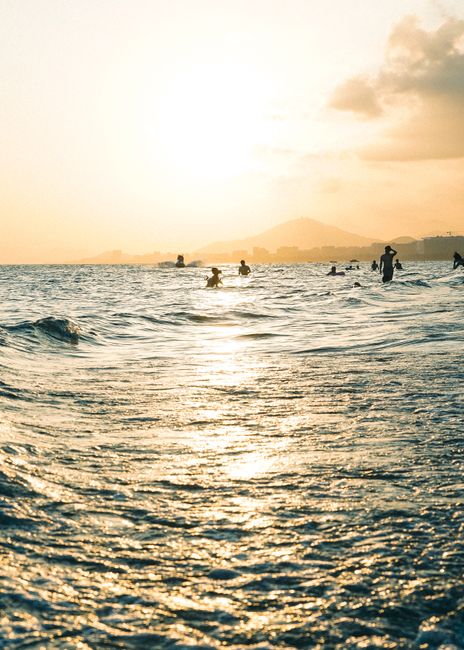 People enjoy a tranquil sunset swim in glistening ocean waters, creating silhouettes against the golden horizon.