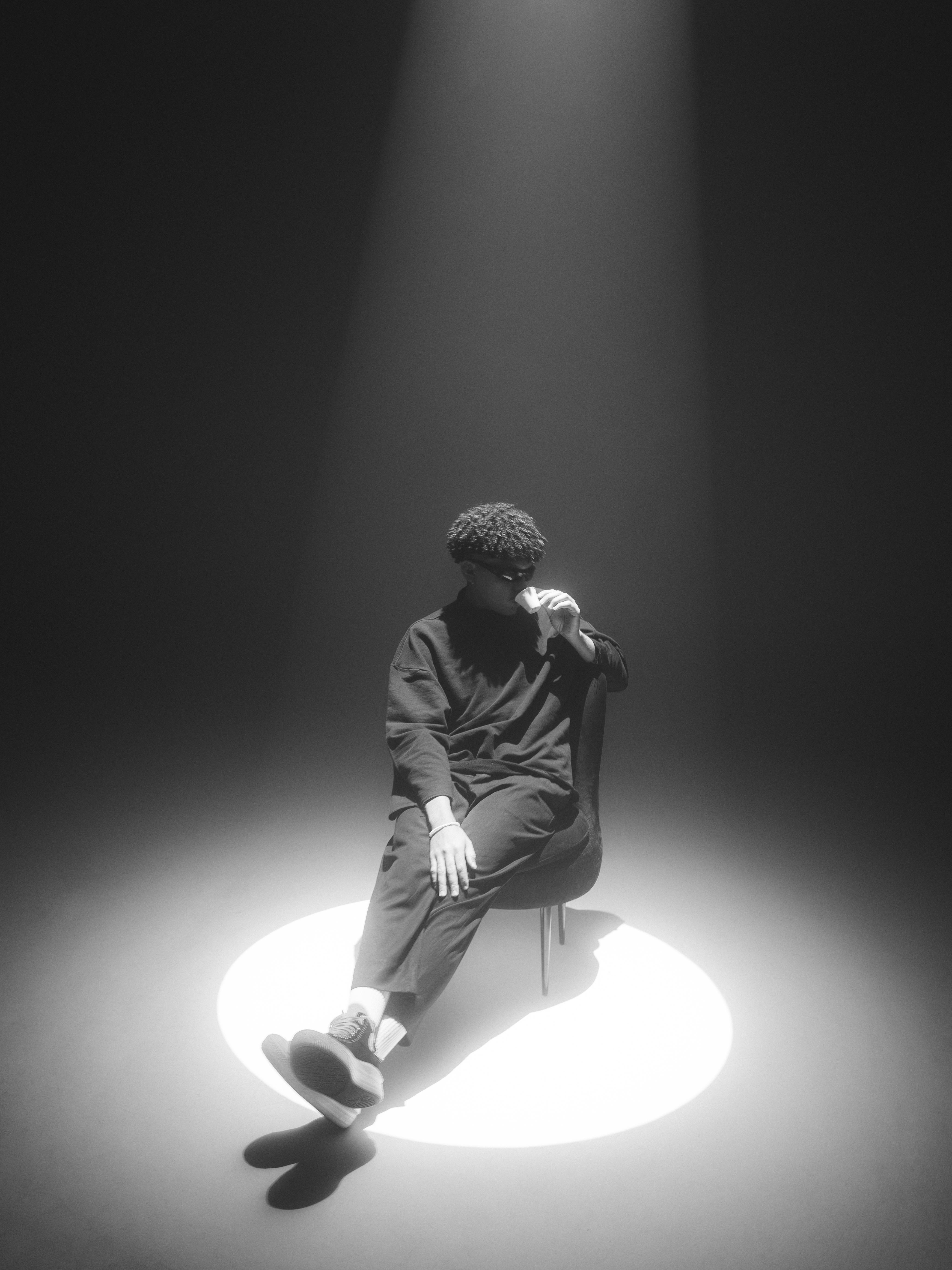 A man sitting on a chair under a spotlight creating a dramatic monochrome scene.