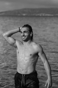 A black and white portrait of a smiling, shirtless man at a Swedish shoreline.