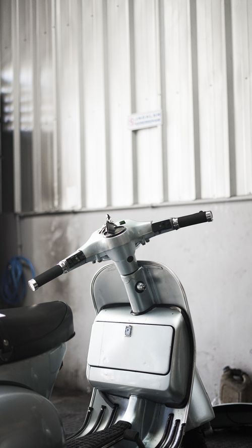 Free Close-up of a classic white scooter parked indoors against corrugated metal. Stock Photo
