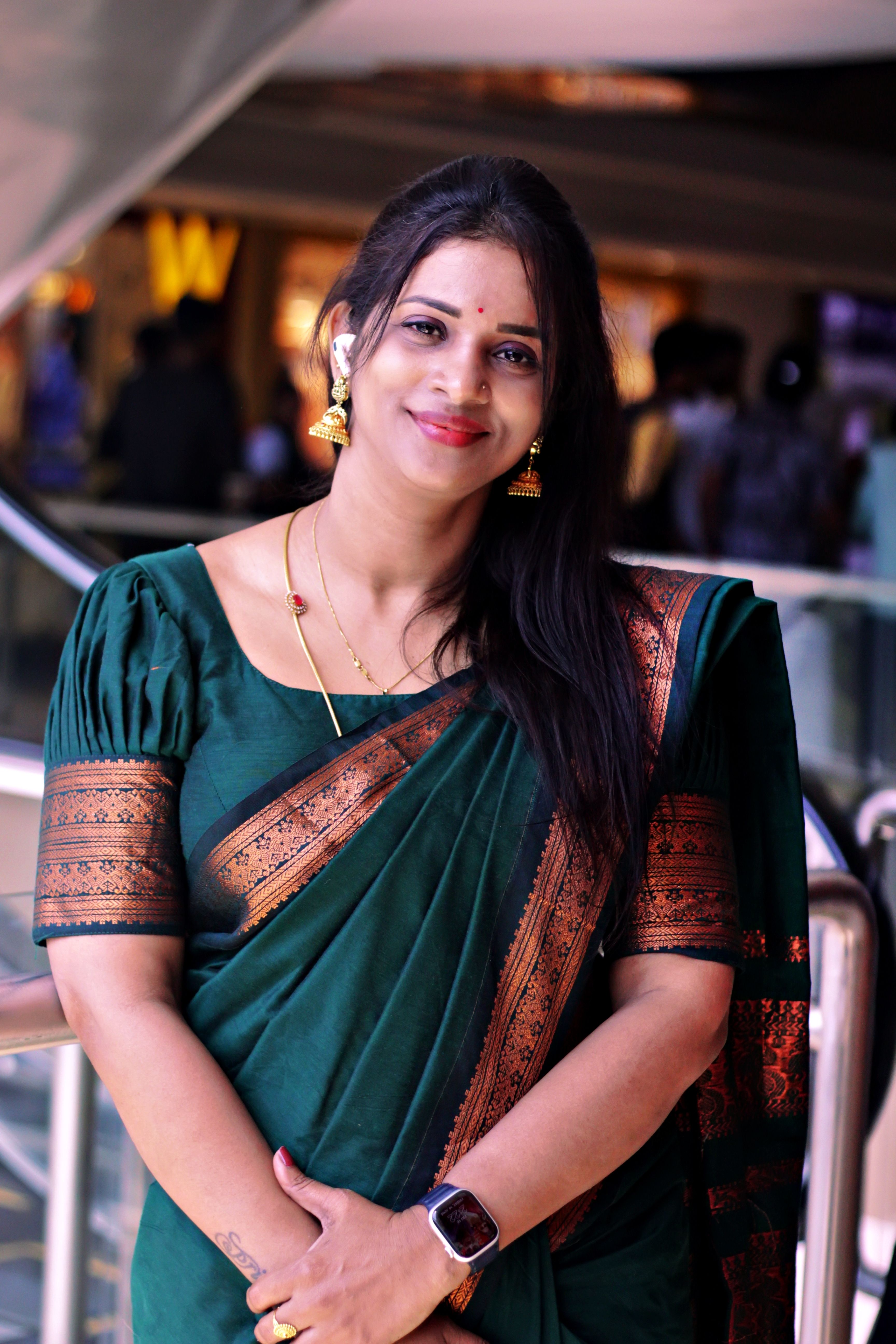 A smiling Indian woman in traditional attire poses elegantly indoors in Puducherry, India.