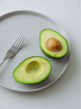 High-quality image of fresh avocado halves on a white plate with a fork, ideal for healthy food concepts.