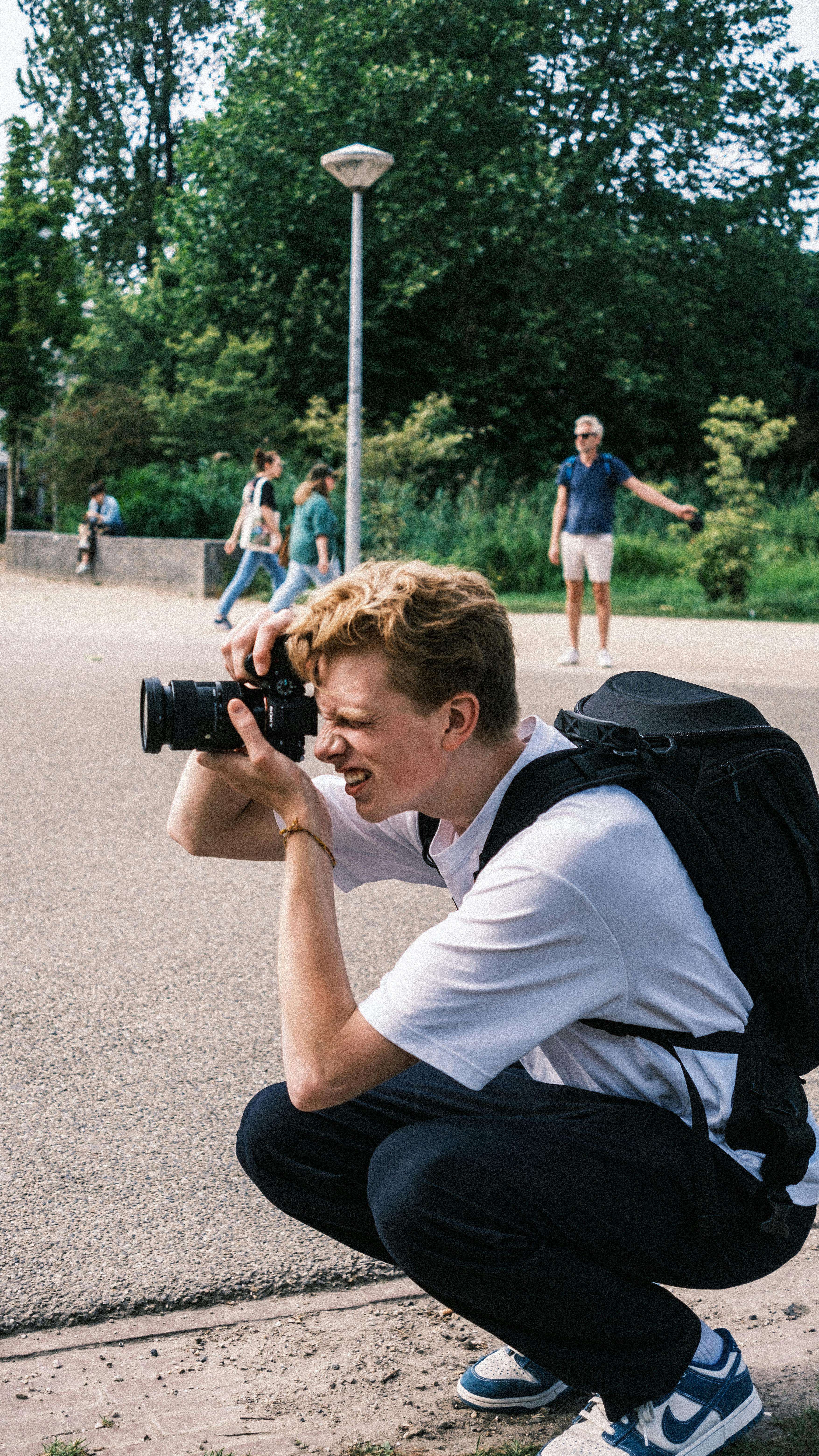 A young male photographer crouches in an urban park capturing moments with his camera.