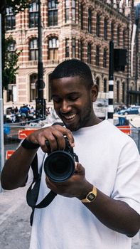 Young man smiling while holding a camera in a vibrant city background, exuding a passion for photography.