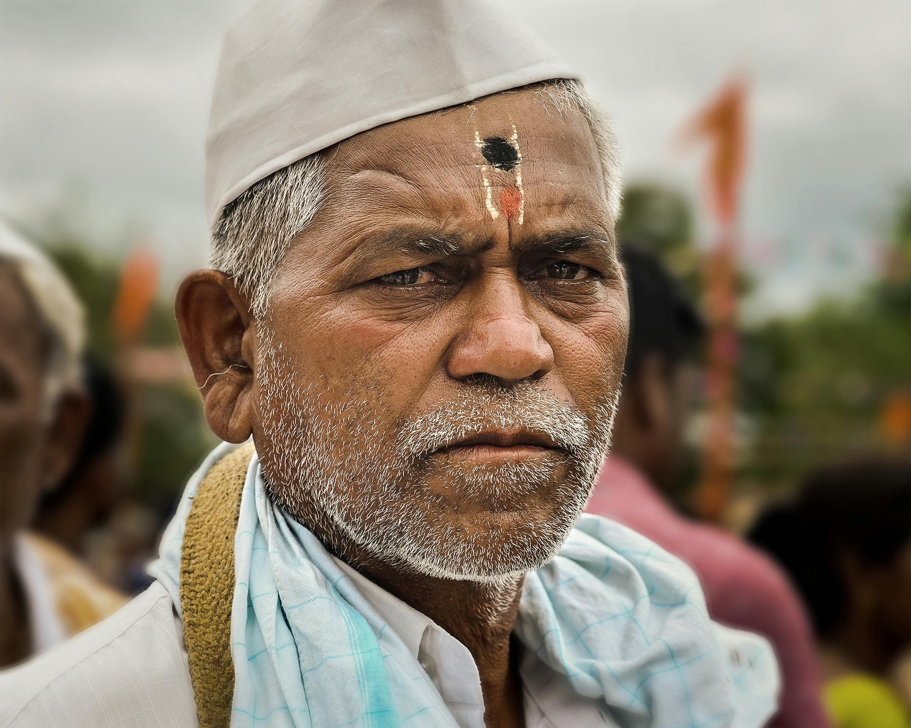Portrait of an elderly Indian man with traditional headwear and facial markings outdoors.