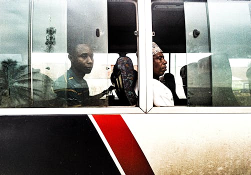Two men sitting on a bus in Zanzibar City, captured through the window showing a typical urban scene.