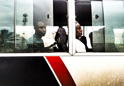 Free Two men sitting on a bus in Zanzibar City, captured through the window showing a typical urban scene. Stock Photo