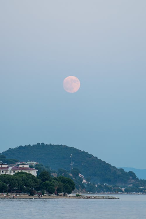 A full moon rising over a small town and water