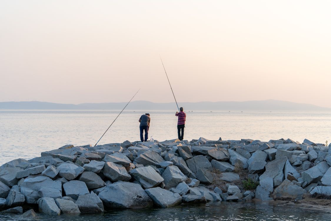 Two people fishing on rocks near the water · Free Stock Photo