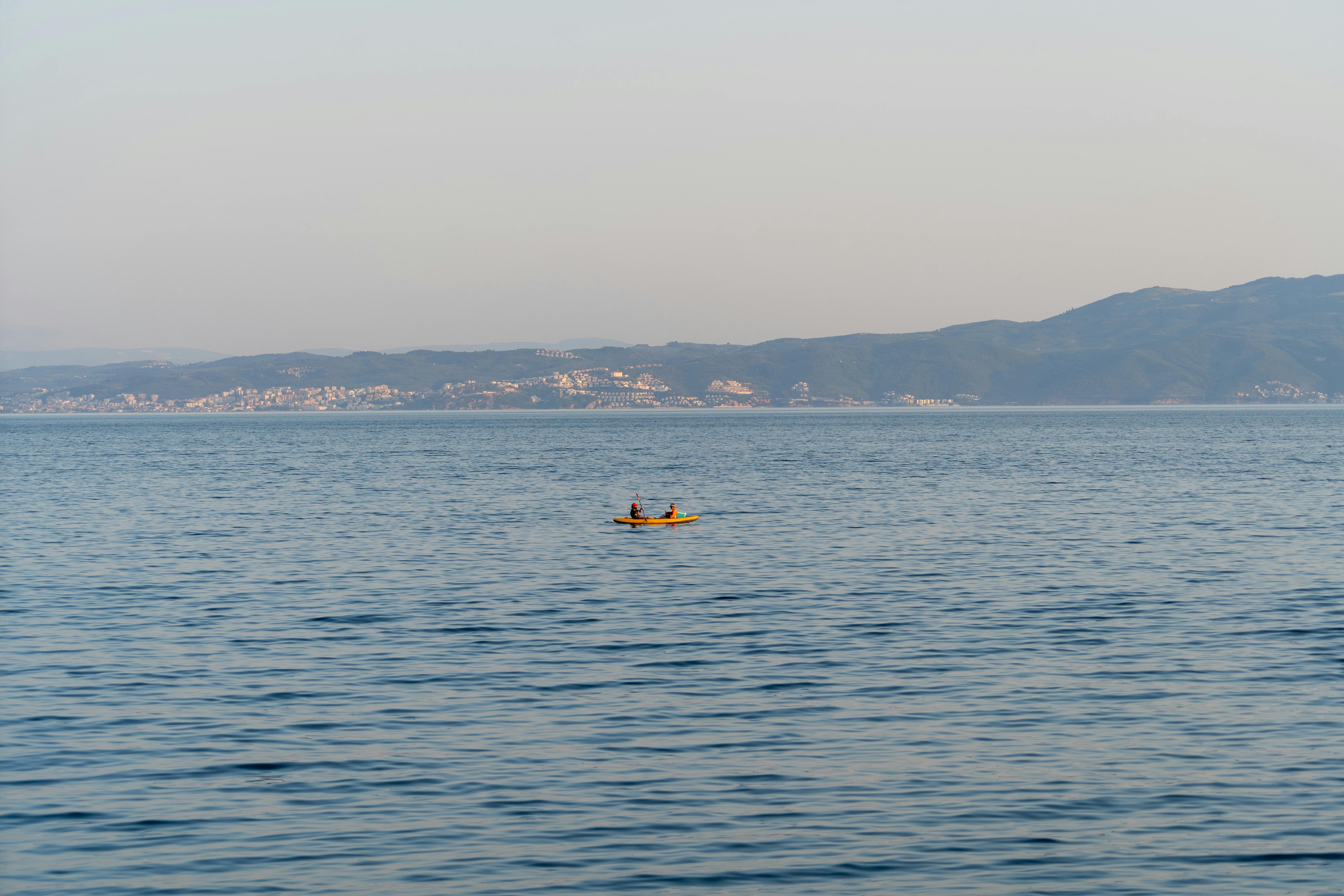 Free A tranquil scene of two people kayaking on calm water with mountains in the background. Stock Photo