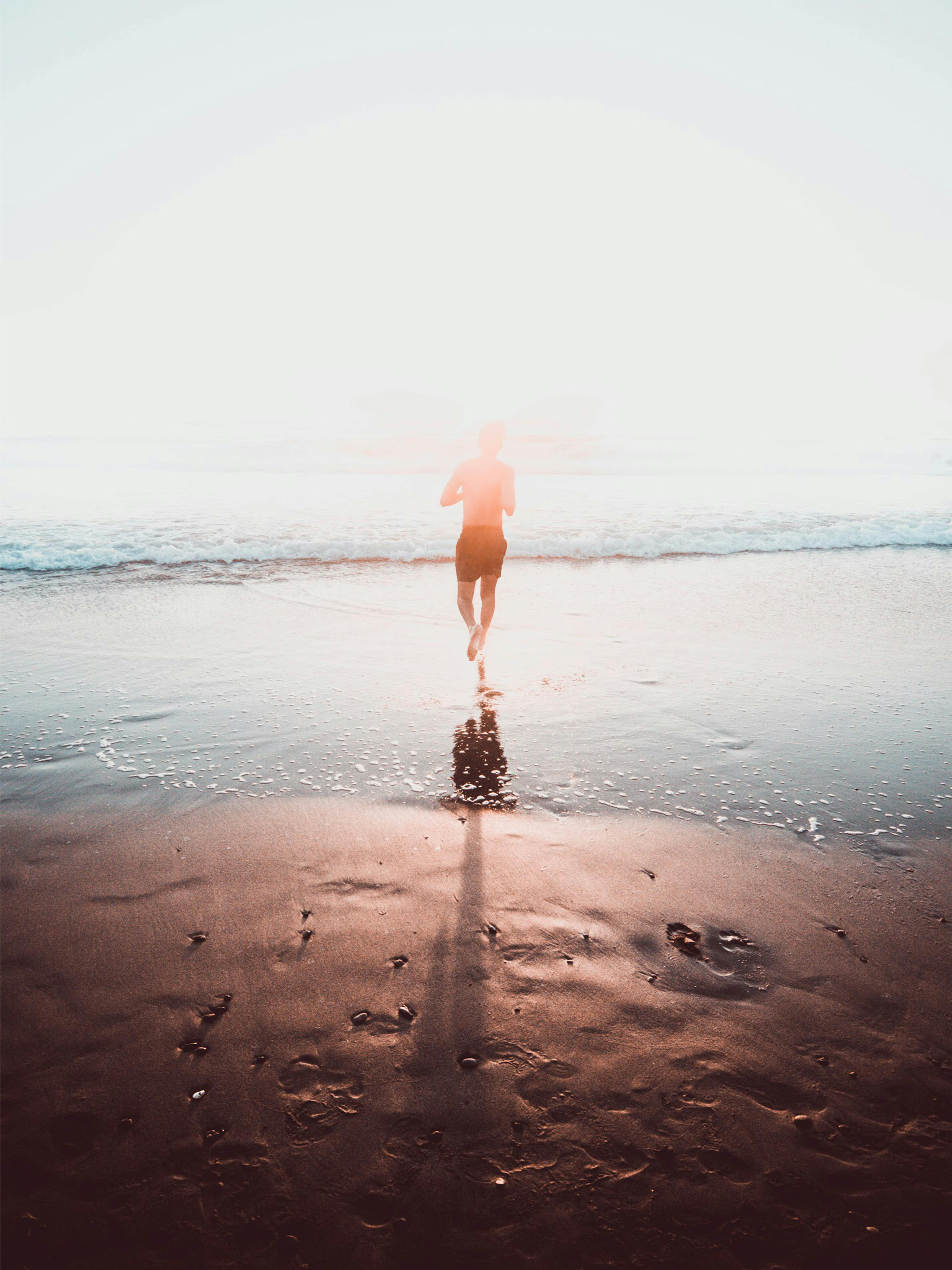 日出时分，一名男子在海滩上奔跑的剪影，在潮湿的沙滩上投下阴影