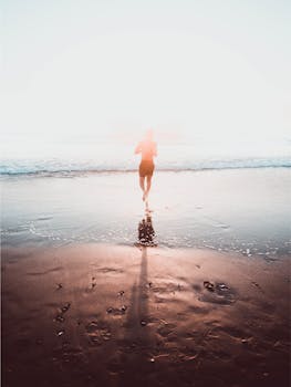 日出时分，一名男子在海滩上奔跑的剪影，在潮湿的沙滩上投下阴影