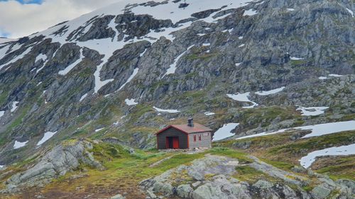 Free A solitary cabin nestled in a rugged, snow-capped mountain, showcasing serene wilderness. Stock Photo