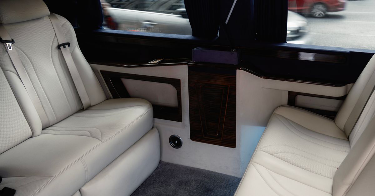 Interior view of a luxury limousine showcasing white leather seating with stylish design and amenities.