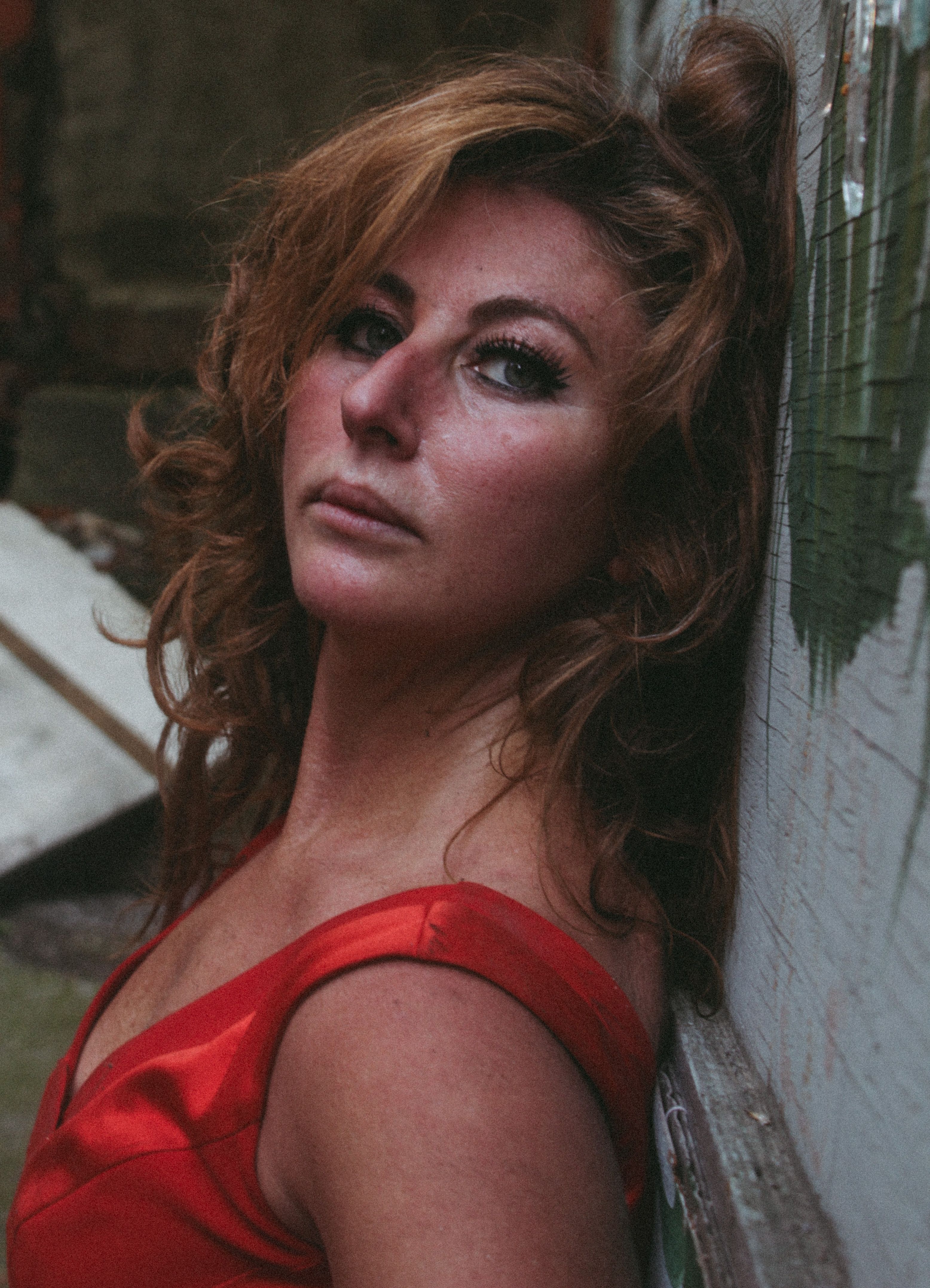 Portrait of a redhead woman wearing a red dress, posing against an urban wall.