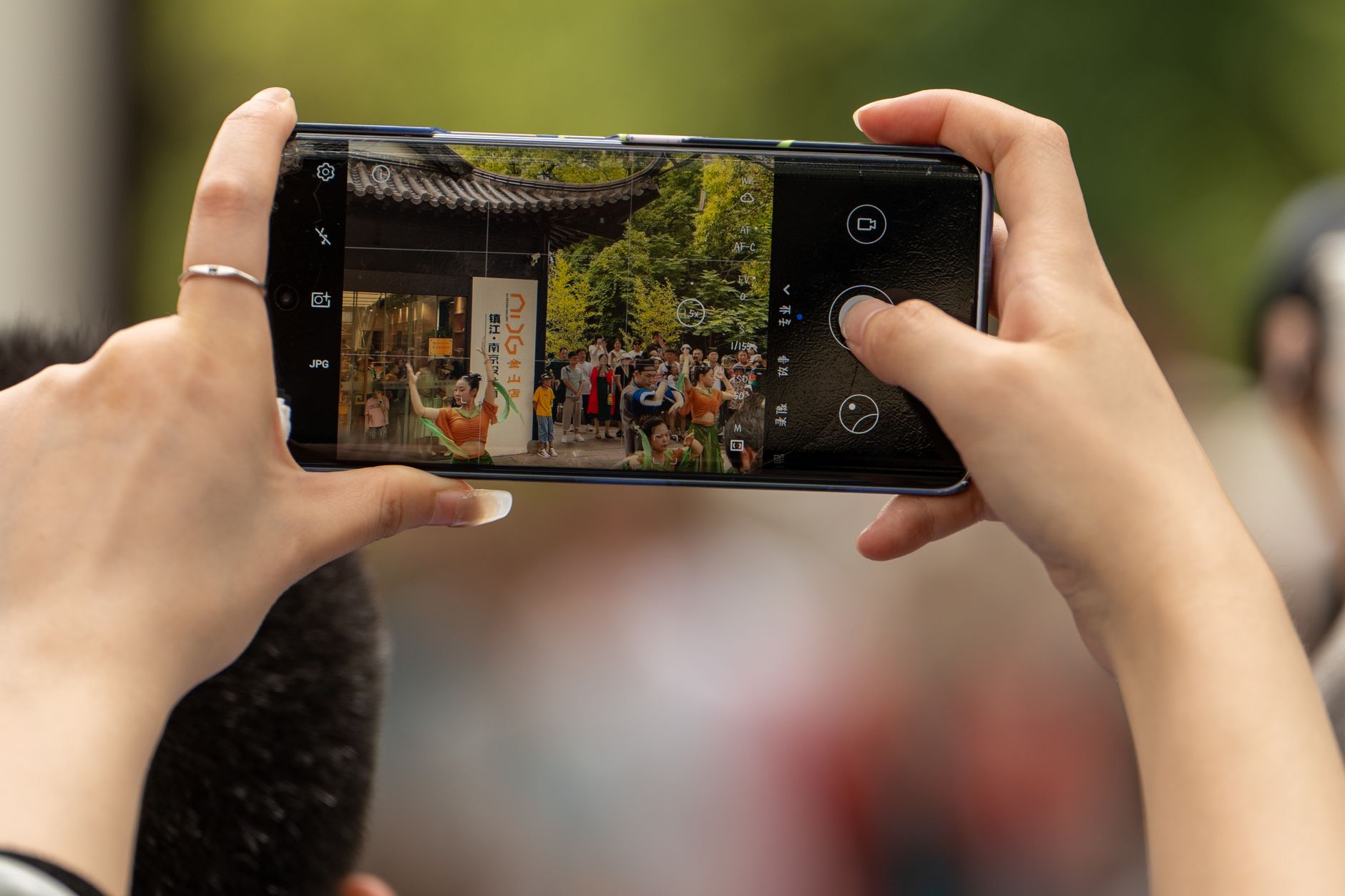 Hands holding a smartphone taking a photo of a cultural event outdoors.