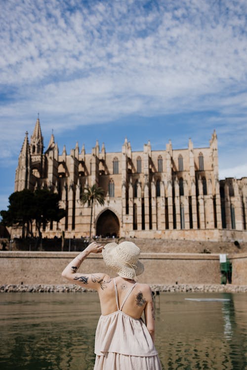 Back View of a Woman Wearing Summer Clothing Looking at Gothic Church by a River