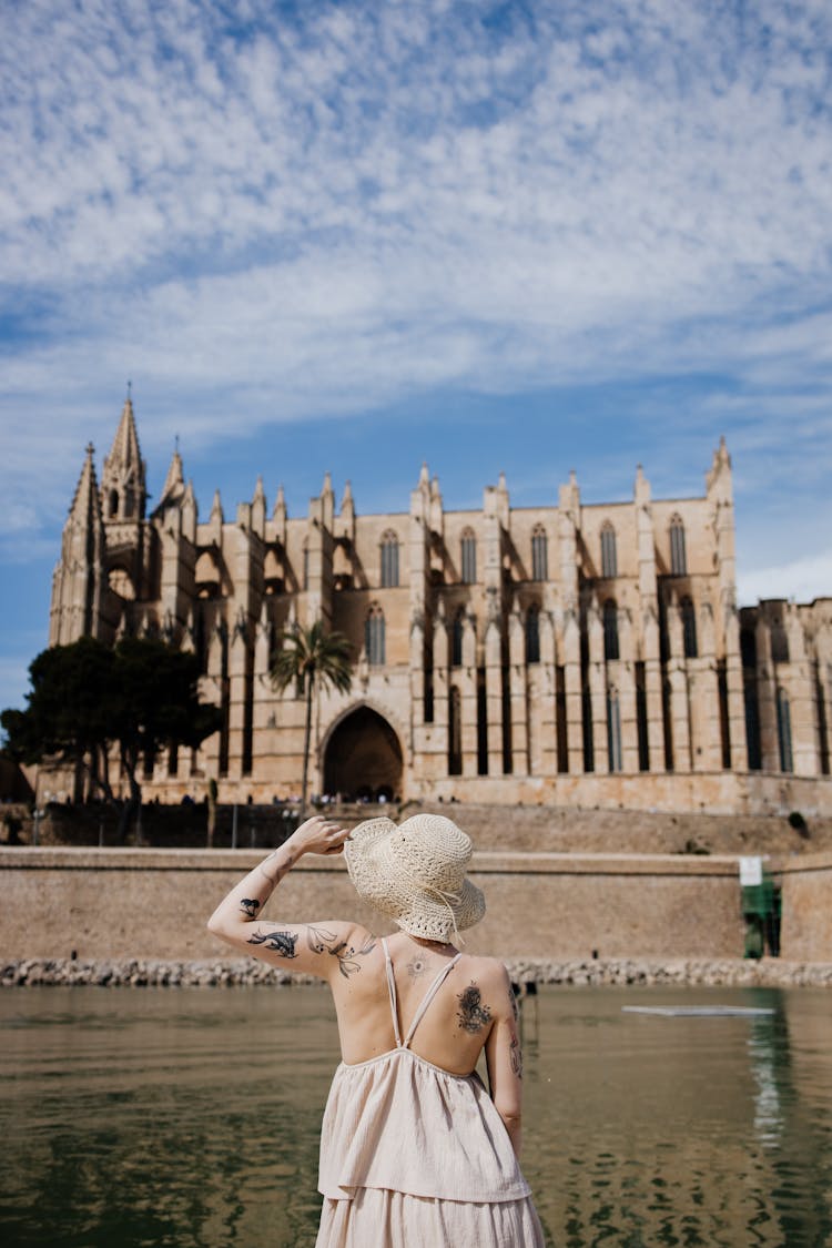 Back View Of A Woman Wearing Summer Clothing Looking At Gothic Church By A River