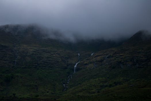 Dramatic misty mountain landscape showcasing cascading waterfalls amidst cloud cover.
