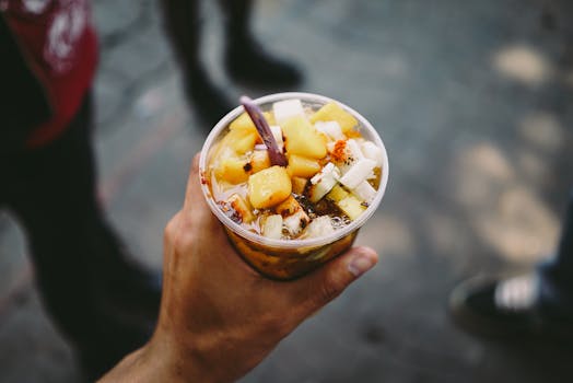 Close-up of a hand holding a cup of colorful Mexican fruit salad outdoors, perfect for a refreshing snack.
