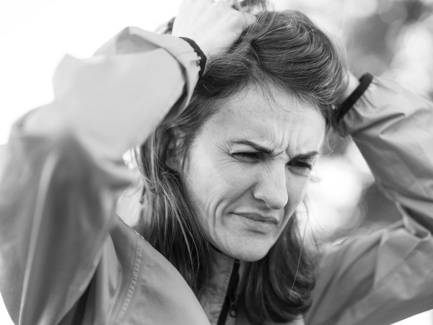 A black and white portrait of a woman outdoors looking pensive and thoughtful.