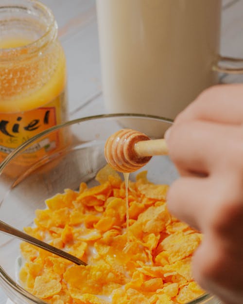 Hand Holding Honey Dipper over Cornflakes