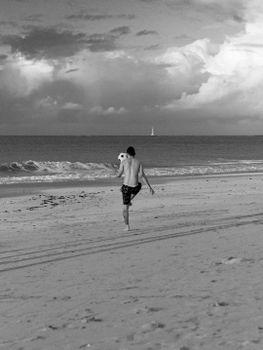 A man showcases his soccer skills on a serene beach with waves in the background.