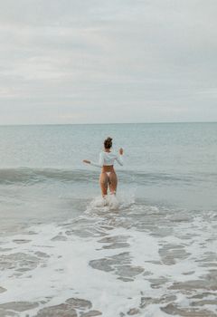 A woman in a white top and bottoms enjoying the calm waves on a serene beach day.