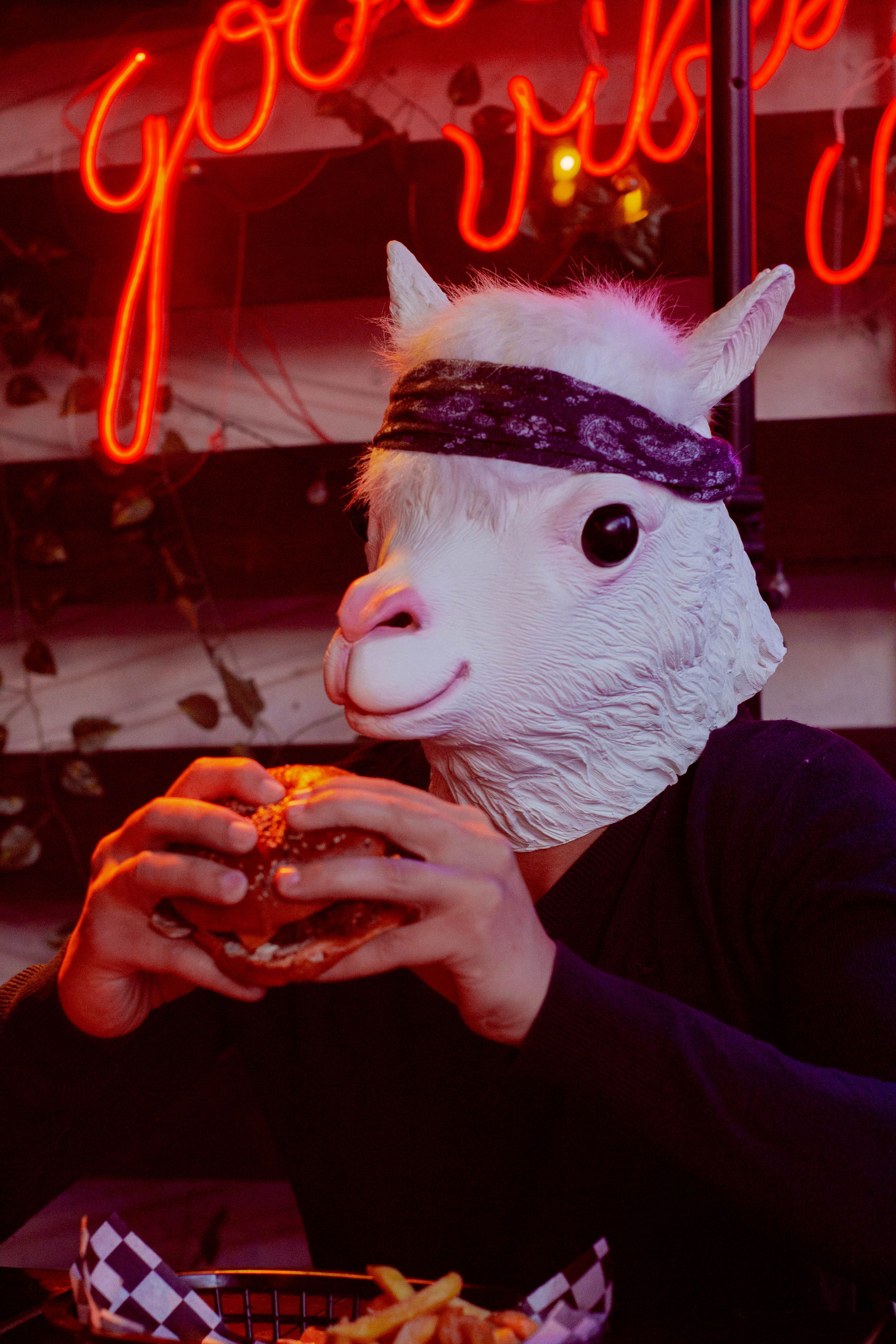 A humorous scene of a person in a llama mask eating a burger in a vibrant indoor setting.