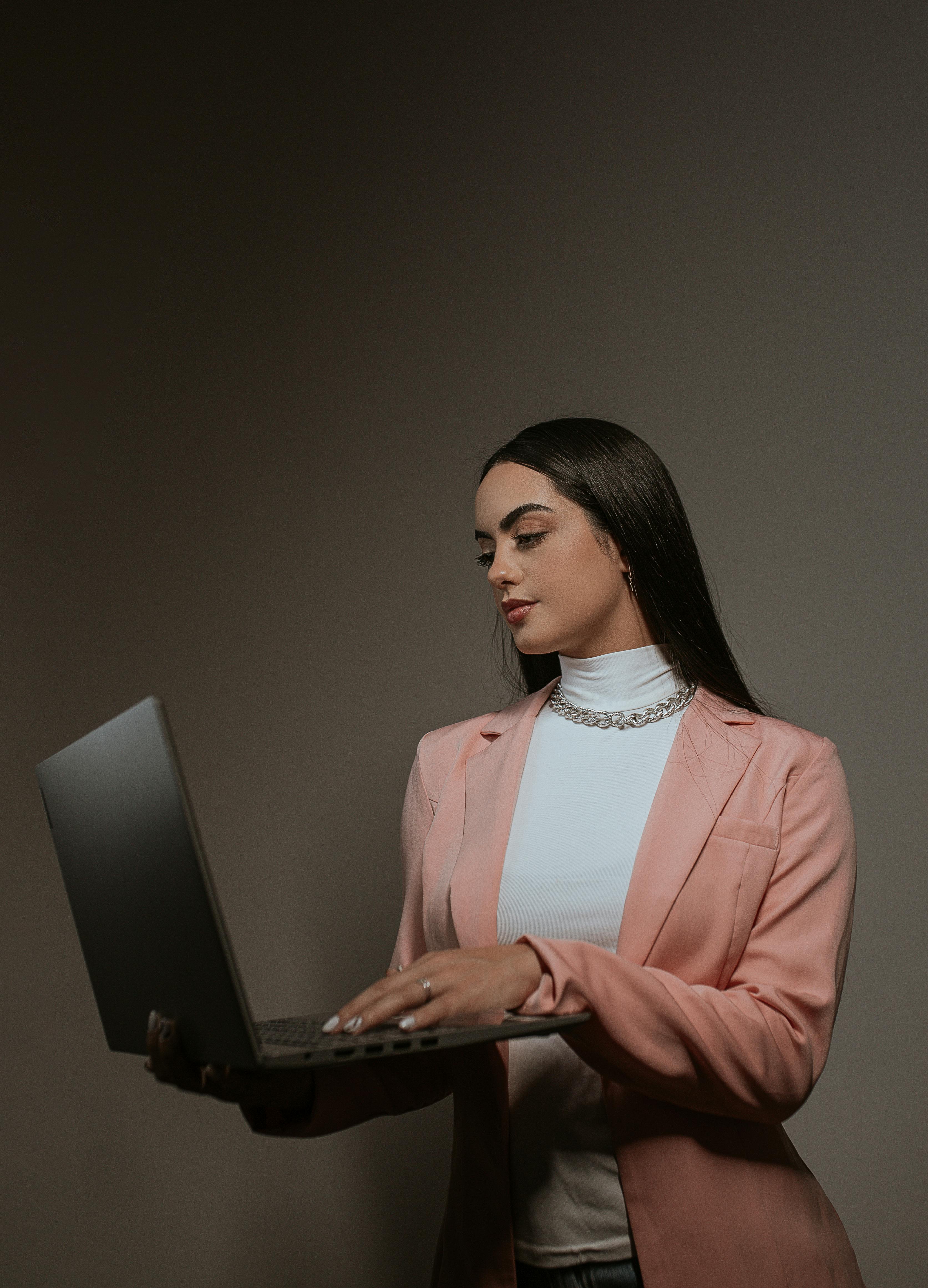 studio shoot of a brunette wearing a pink suit using laptop against gray background