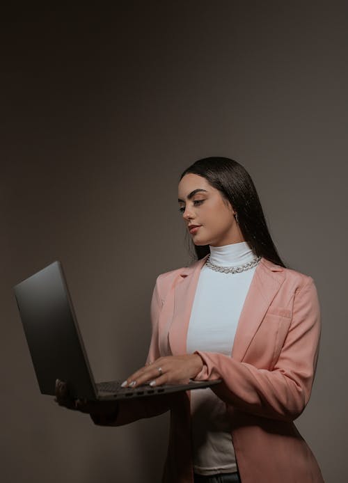 Studio Shoot of a Brunette Wearing a Pink Suit Using Laptop against Gray Background