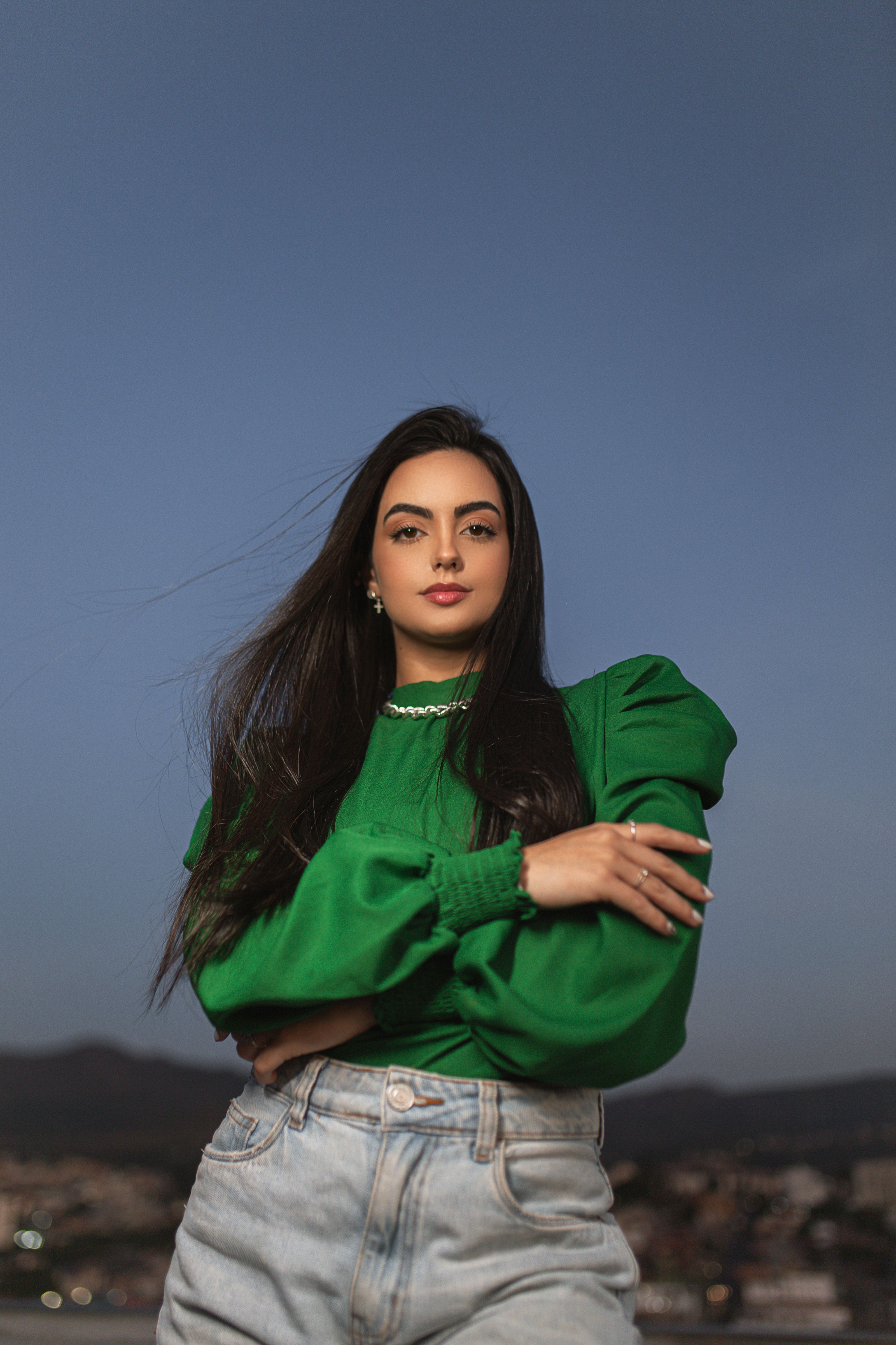 Mulher estilosa em blusa verde e jeans posando confiantemente ao ar livre.
