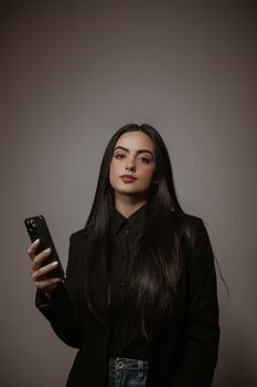 Elegant woman in black clothing using a smartphone in a studio setting.