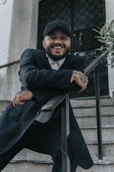 Confident man with beard and mustache smiling, leaning on a railing outdoors.