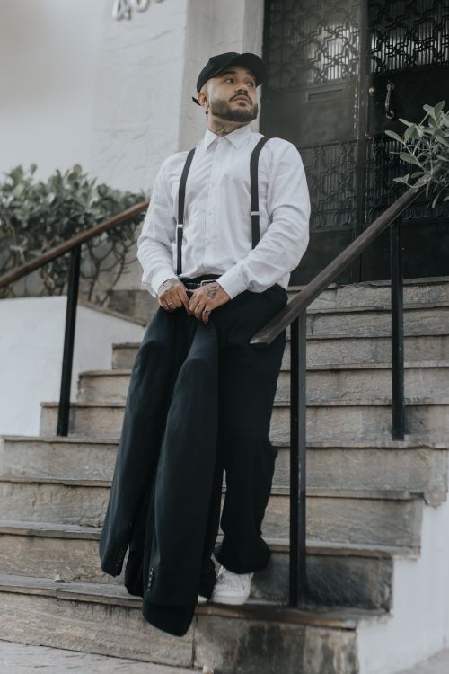 Free A man dressed in vintage fashion, including suspenders and a cap, stands on an outdoor staircase. Stock Photo