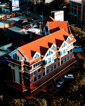 Aerial view of a unique urban building with a striking red roof and surrounding cityscape.