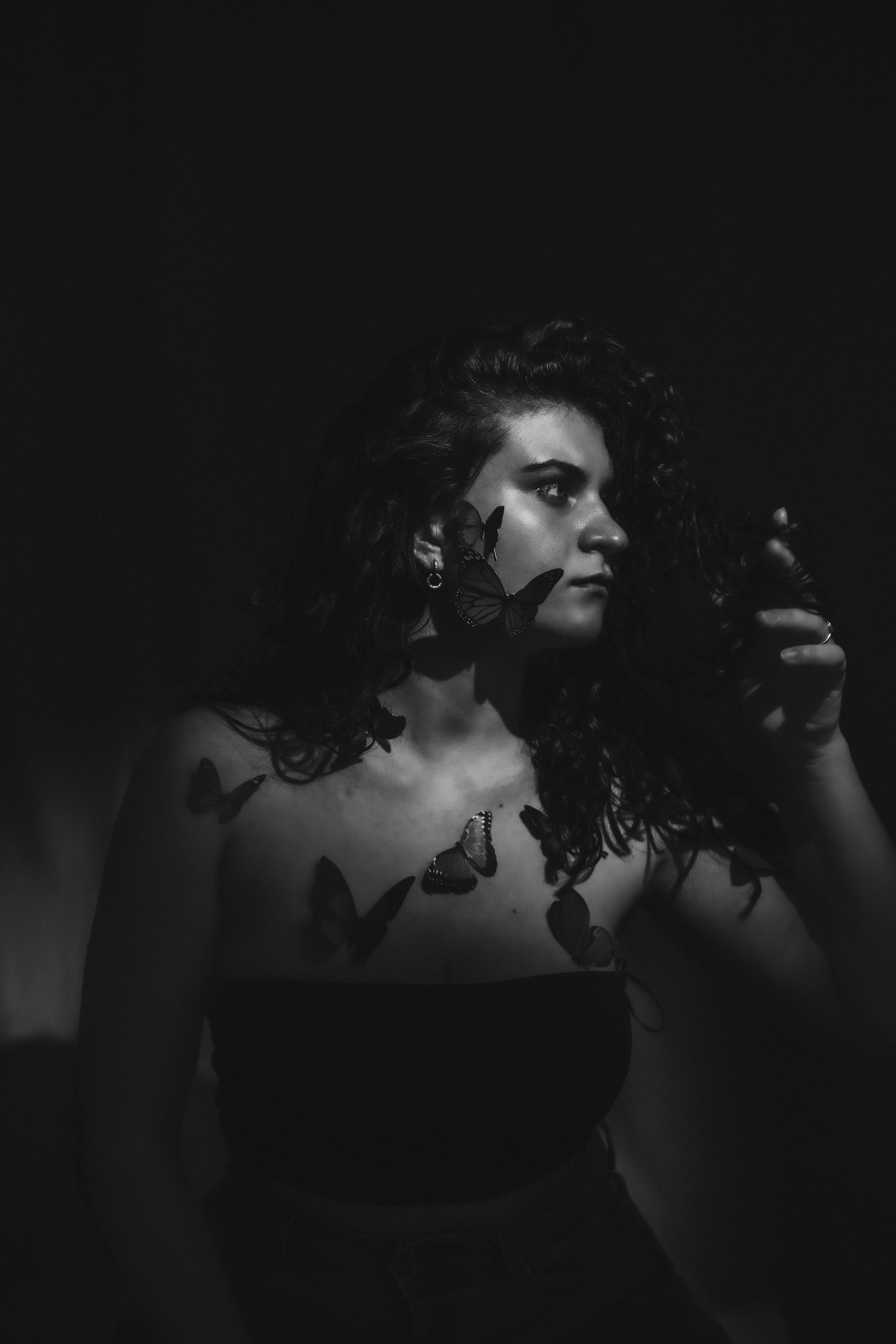 Dark and artistic black and white portrait of a woman adorned with butterflies.