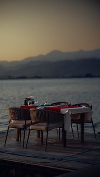 Elegant outdoor dining setup on a pier at sunset overlooking calm ocean waters.
