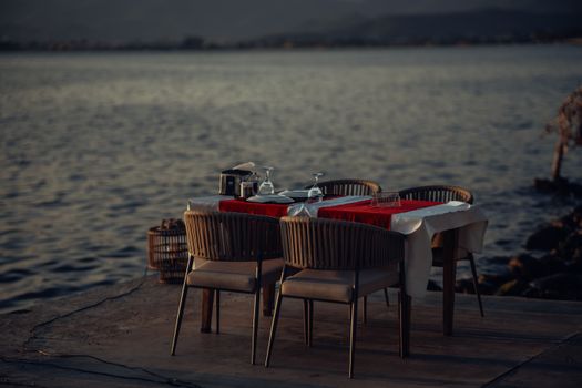 Elegant dining setup on a pier by the sea at sunset, perfect for romantic evenings.