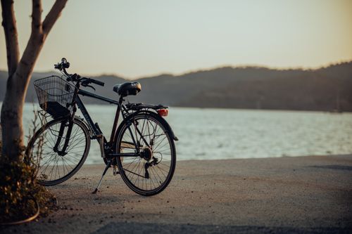 Free A serene image of a bicycle parked by the waterside during a picturesque sunset, perfect for serene moments. Stock Photo