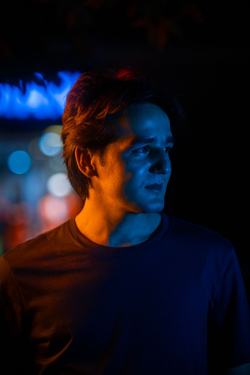 Dramatic portrait of a young man with colorful lights in a nighttime scene.
