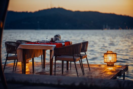 Cozy outdoor dining setup on a lakeside dock during a beautiful sunset, perfect for romantic moments.