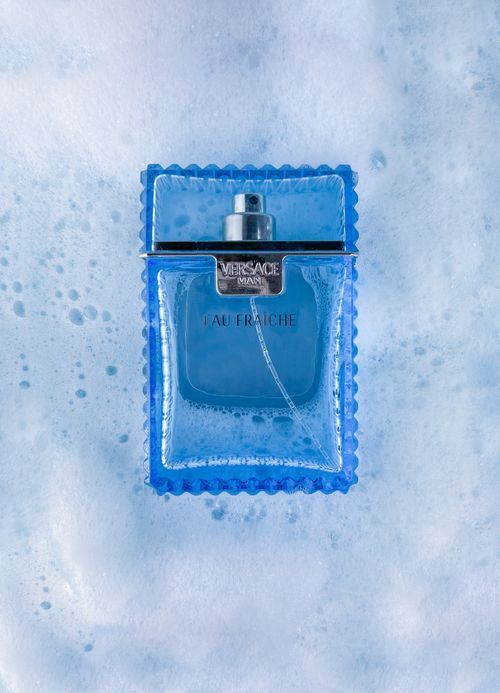 Free Close-up of a luxury blue glass perfume bottle resting on a foamy surface. Stock Photo