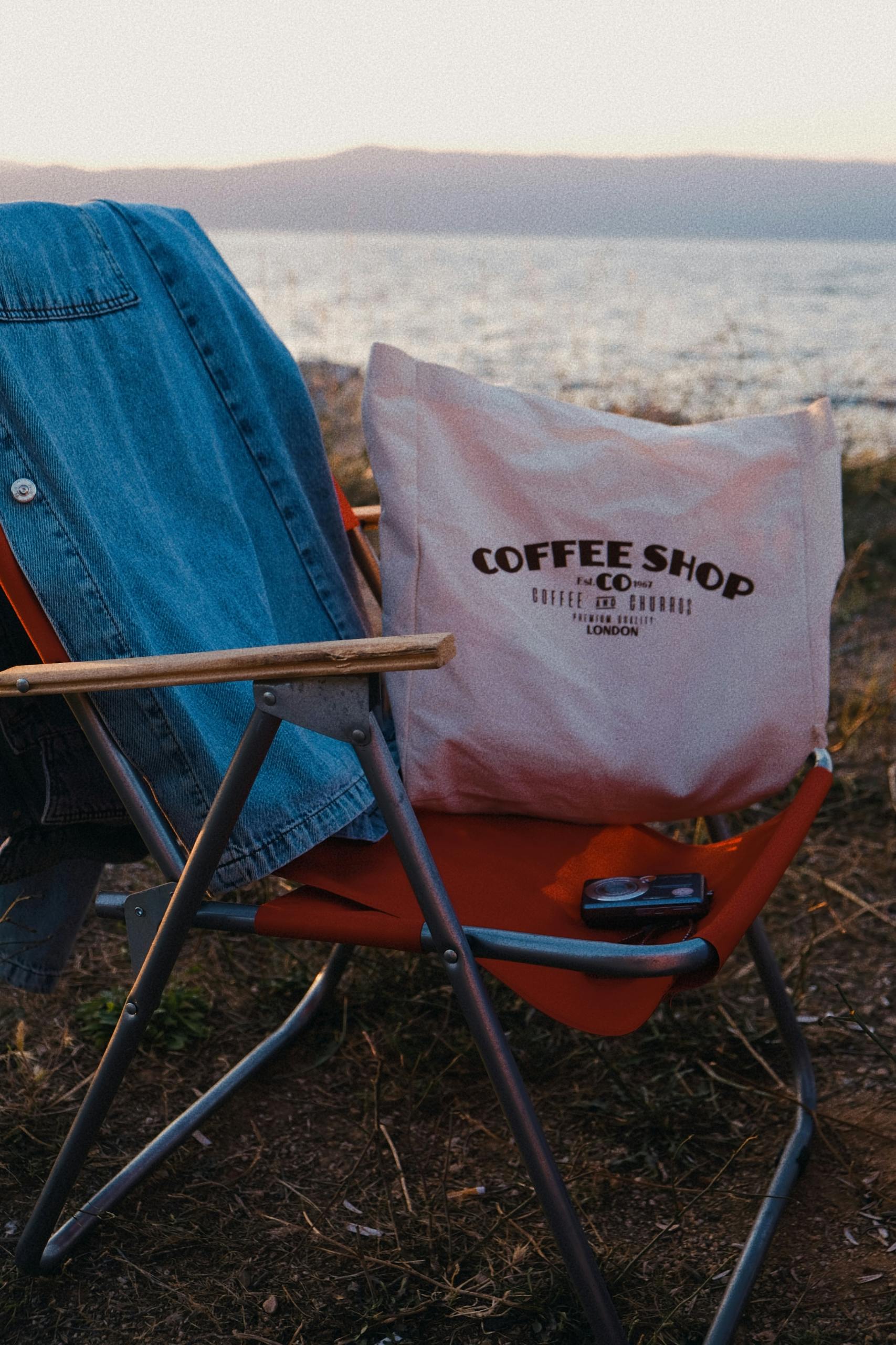 A chair with a denim jacket and a tote bag sits by the water's edge, capturing a peaceful outdoor scene.